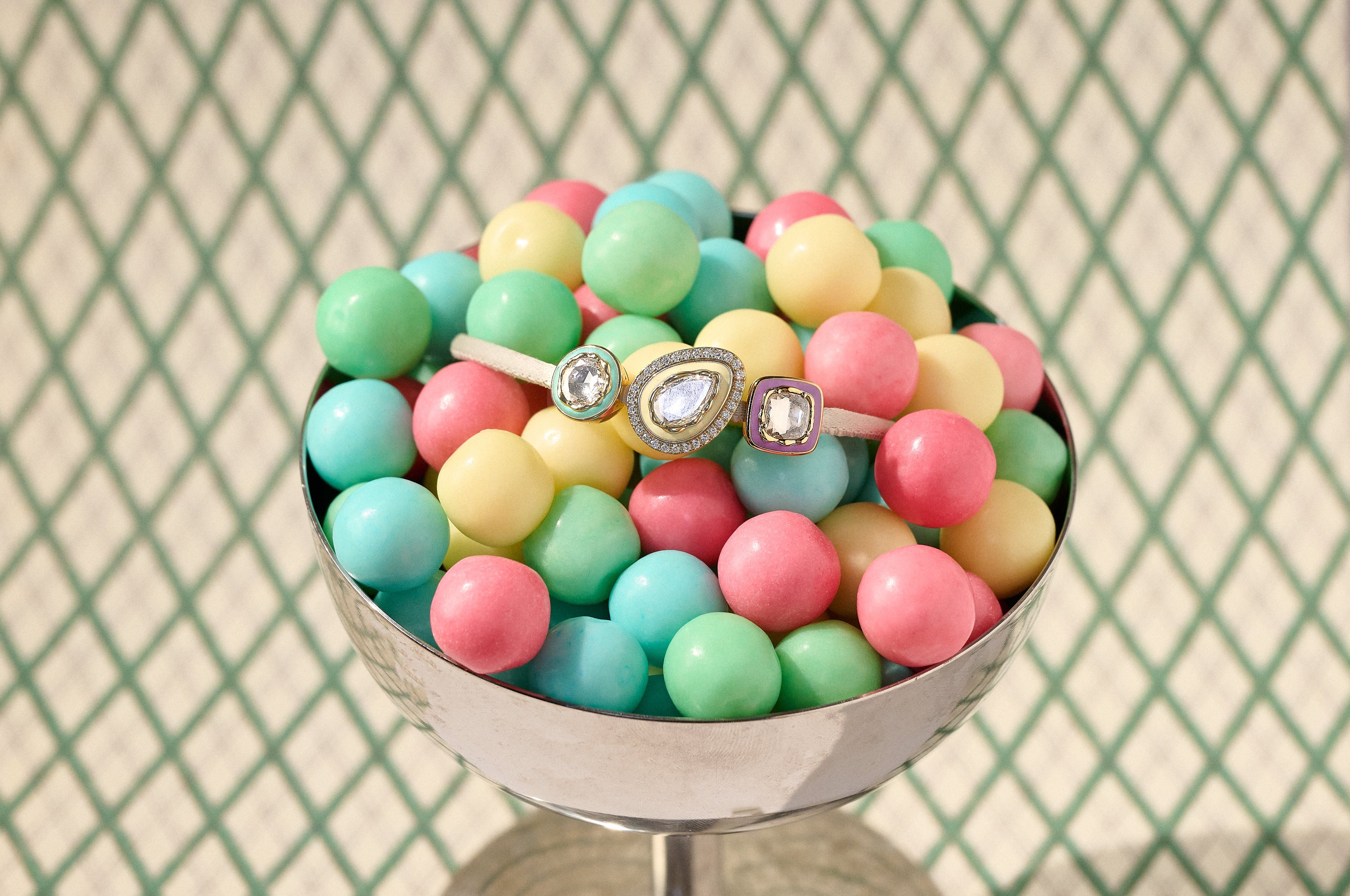 Pastel-colored bubblegum  in a vintage silver dish with diamond bracelet inside on a patterned background