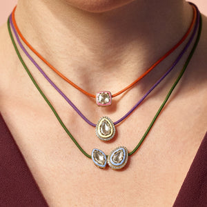 Close-up of a person wearing multiple necklaces with colourful cords and unique diamond pendants.
