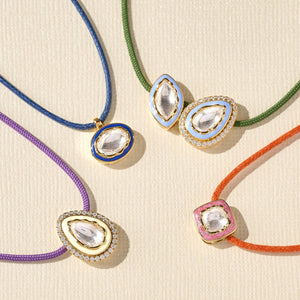 Colourful diamond necklaces with teardrop-shaped pendants on a beige background