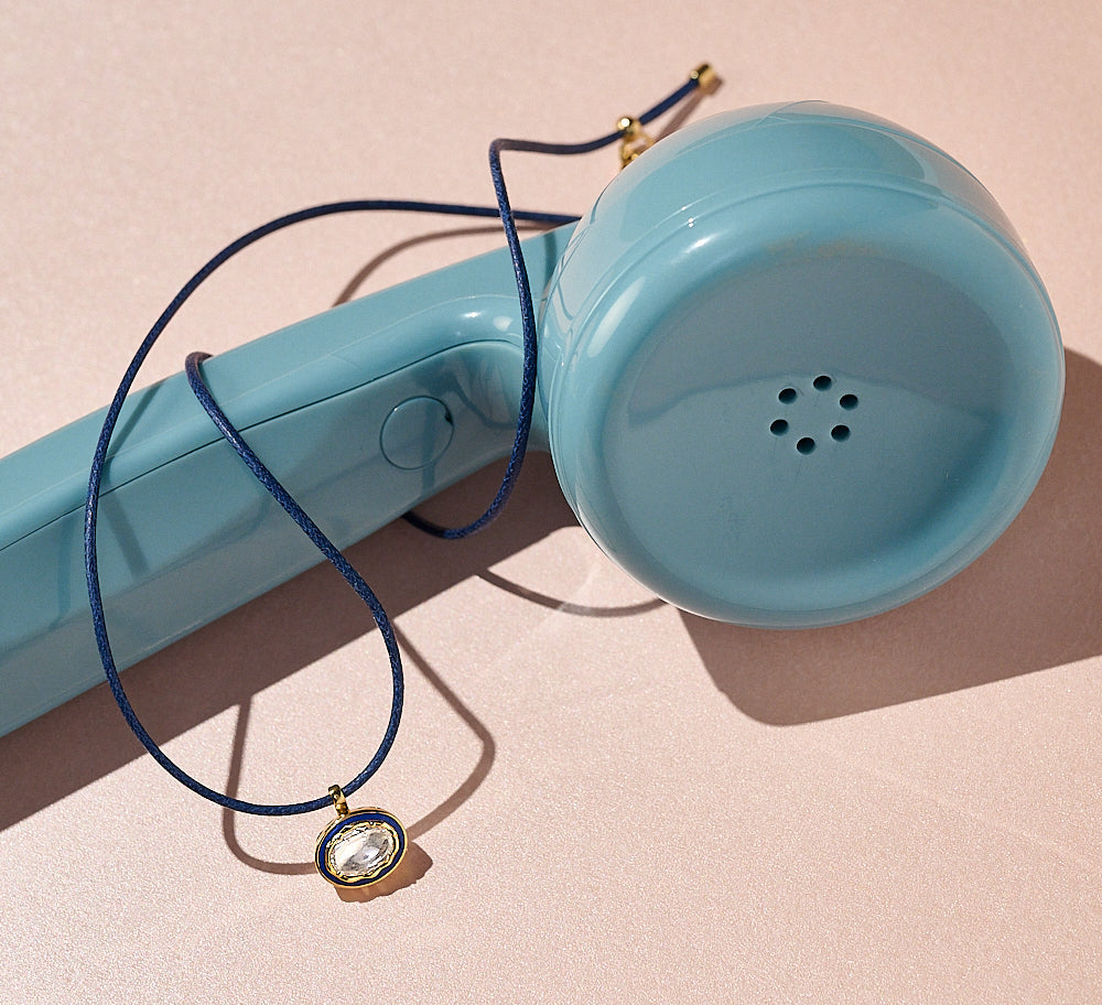 Blue vintage phone with a diamond cord necklace on a pink background